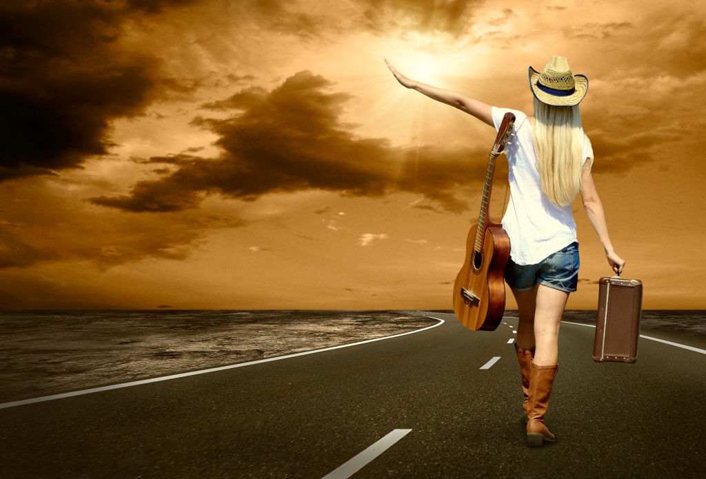 Young woman with guitar on the road and her vintage baggage